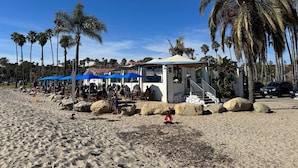 Ein Restaurant direkt am Strand mit Terrassensitzplätzen, Palmen und einem Rettungsturm.