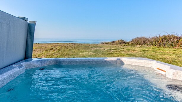 A hot tub with a clear view of the ocean and grassy area.