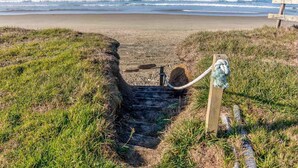 A beach path leading to the ocean with a wooden bench and a rope barrier.