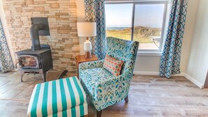 A cozy room with a stone wall, a sofa with a patterned cover, a striped ottoman, a lamp, and a view of the outdoors through a window.