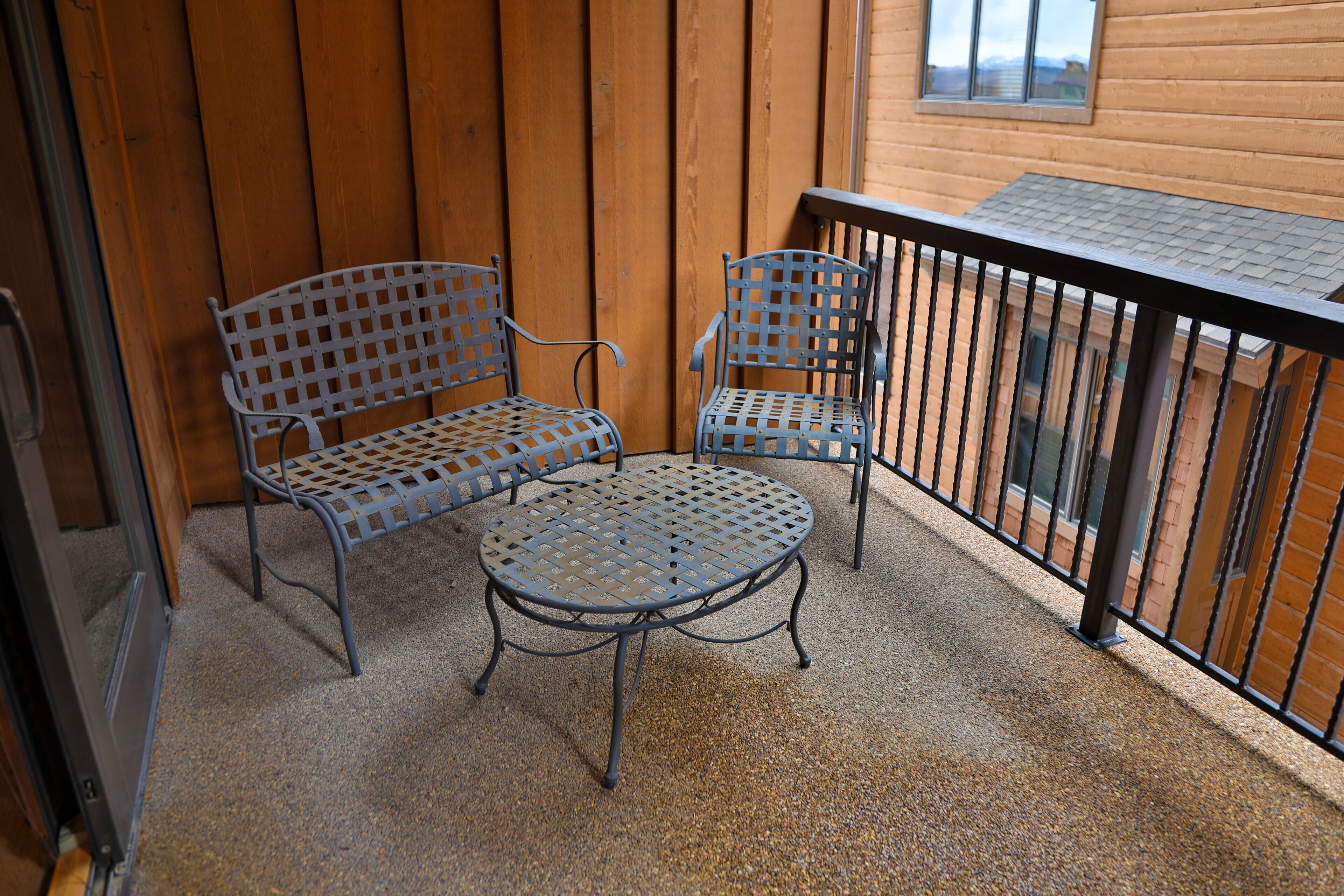 Ein Balkon mit zwei Metallstühlen, einem kleinen Tisch, Holzwänden und einem Metallgeländer.