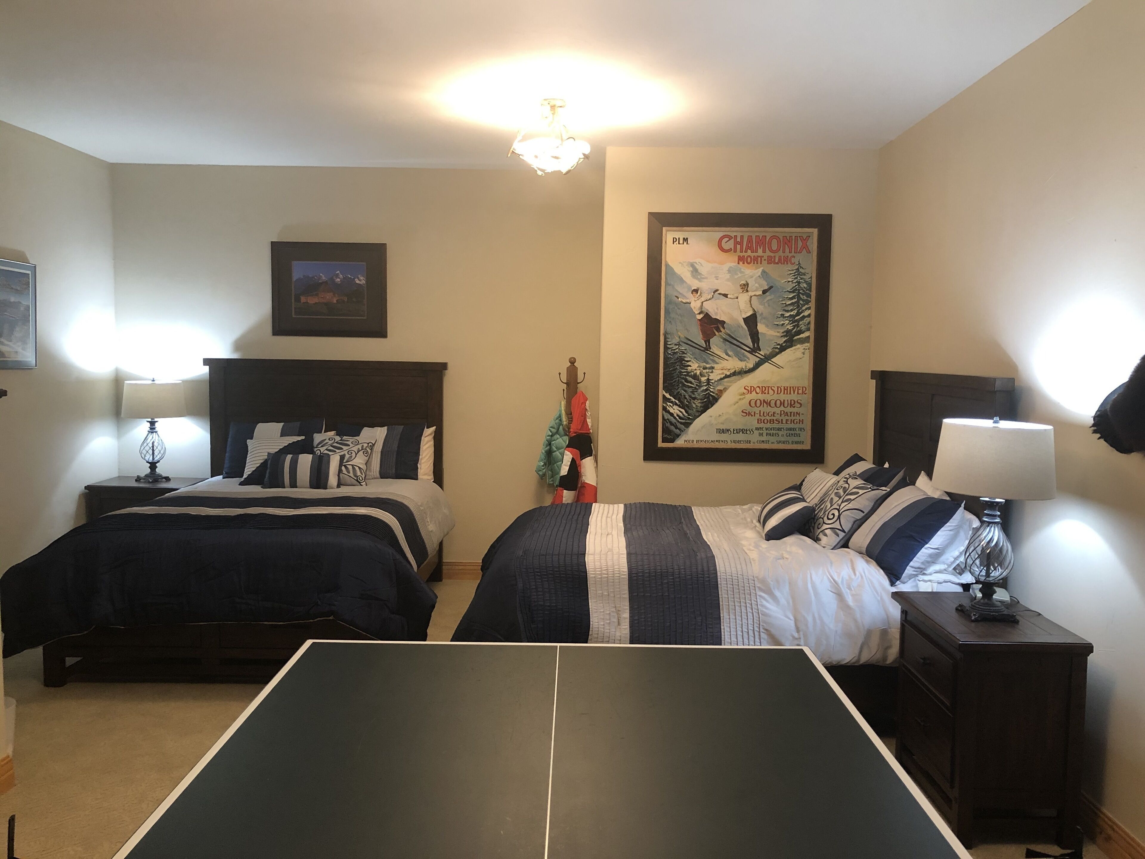 A hotel room with two beds, a ping pong table, a framed poster on the wall, and a chandelier.