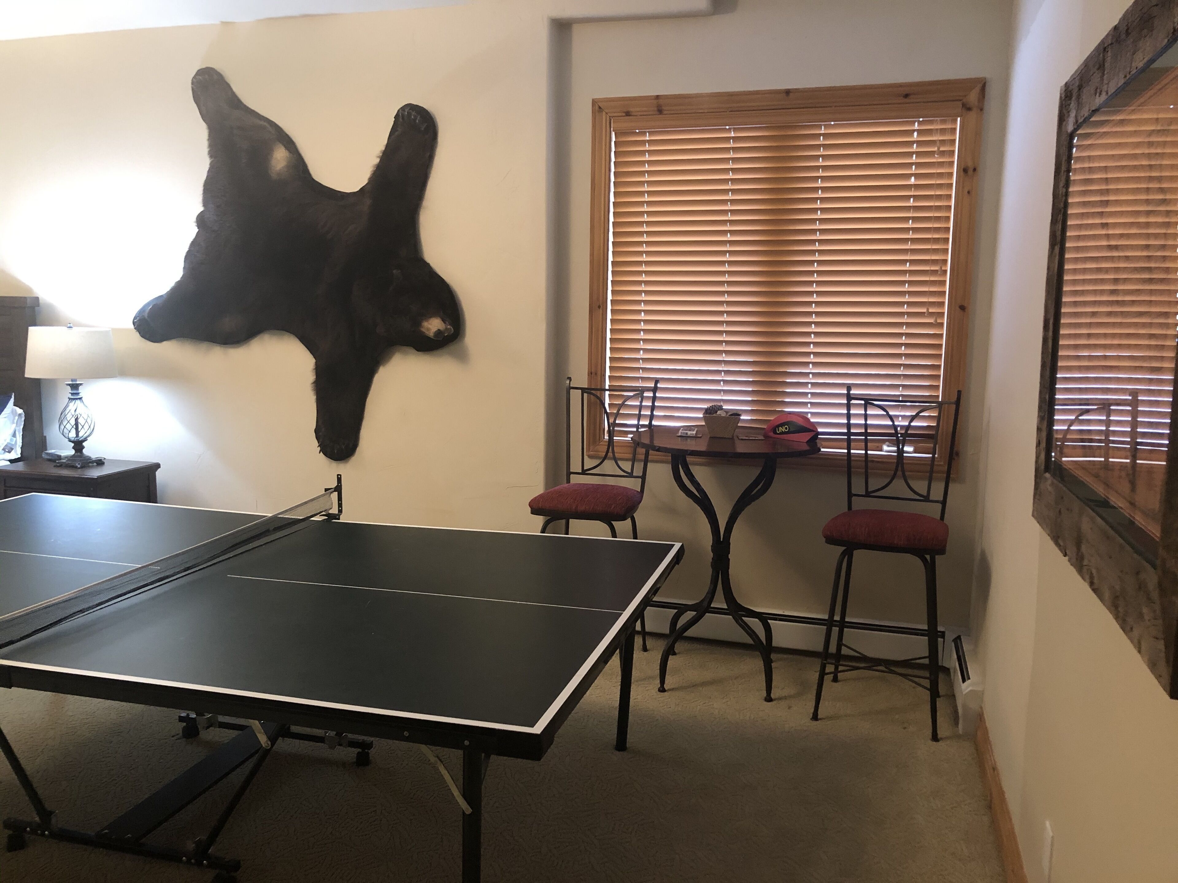 A ping pong table, two chairs, a table with a basket and a phone, and a window with blinds.