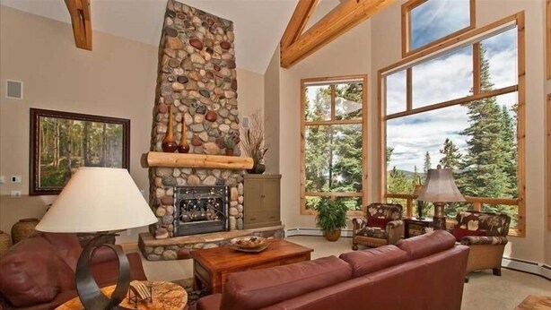 A cozy living room with a stone fireplace, leather sofas, and large windows offering a view of trees. - Luxury Home, Family Friendly, 4900 Sq Foot, 6 BR Ski in/Out! (Breckenridge)