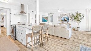 A modern kitchen with a central island, a dining area with a sofa and chairs, and a living room with a large TV and artwork.