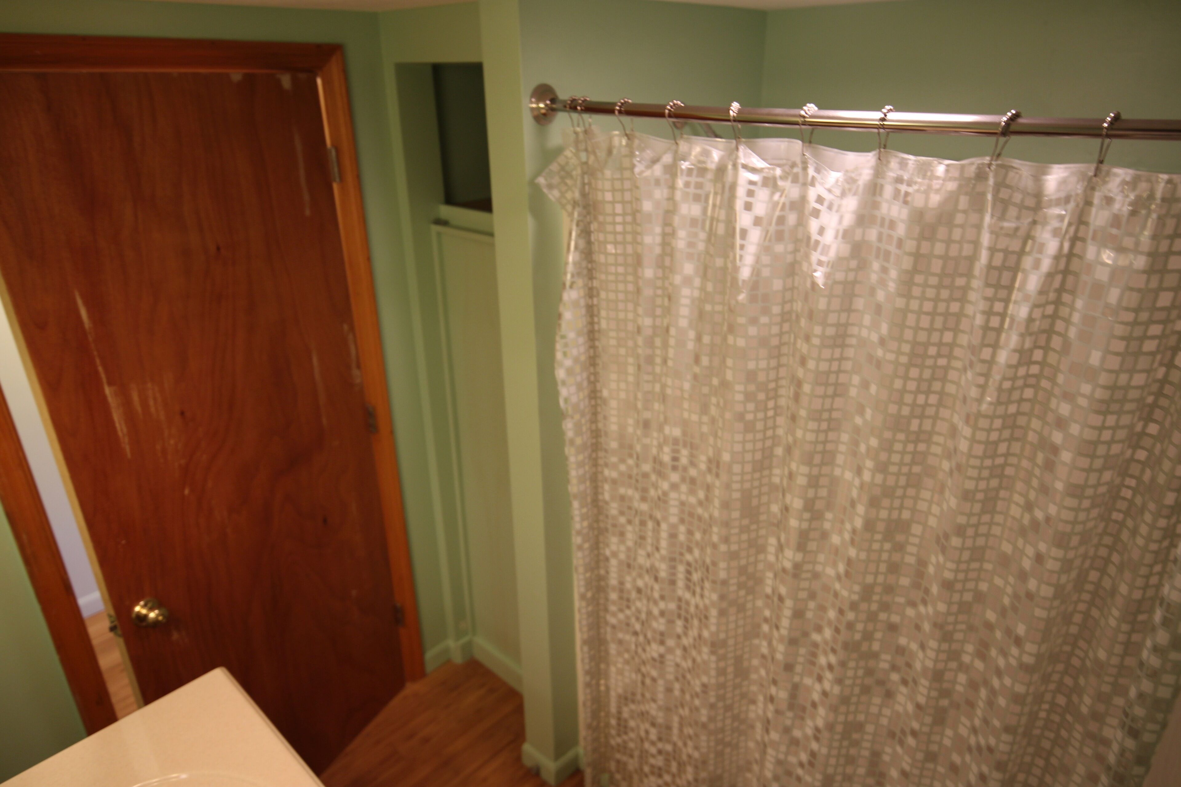A bathroom with a wooden door, a shower curtain with a checkered pattern, and a white sink.