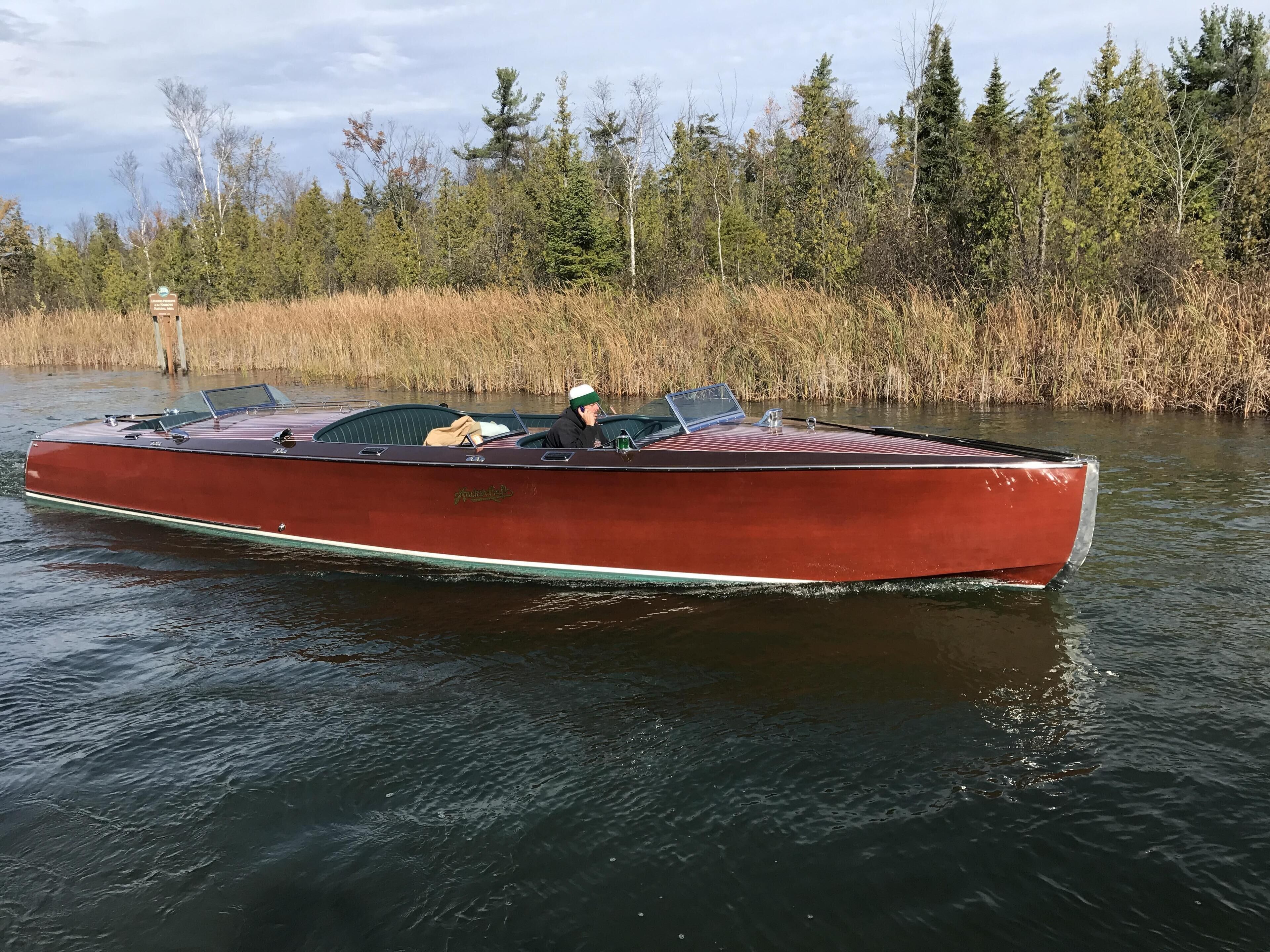 A red motorboat on calm water with a forested shoreline in the background.