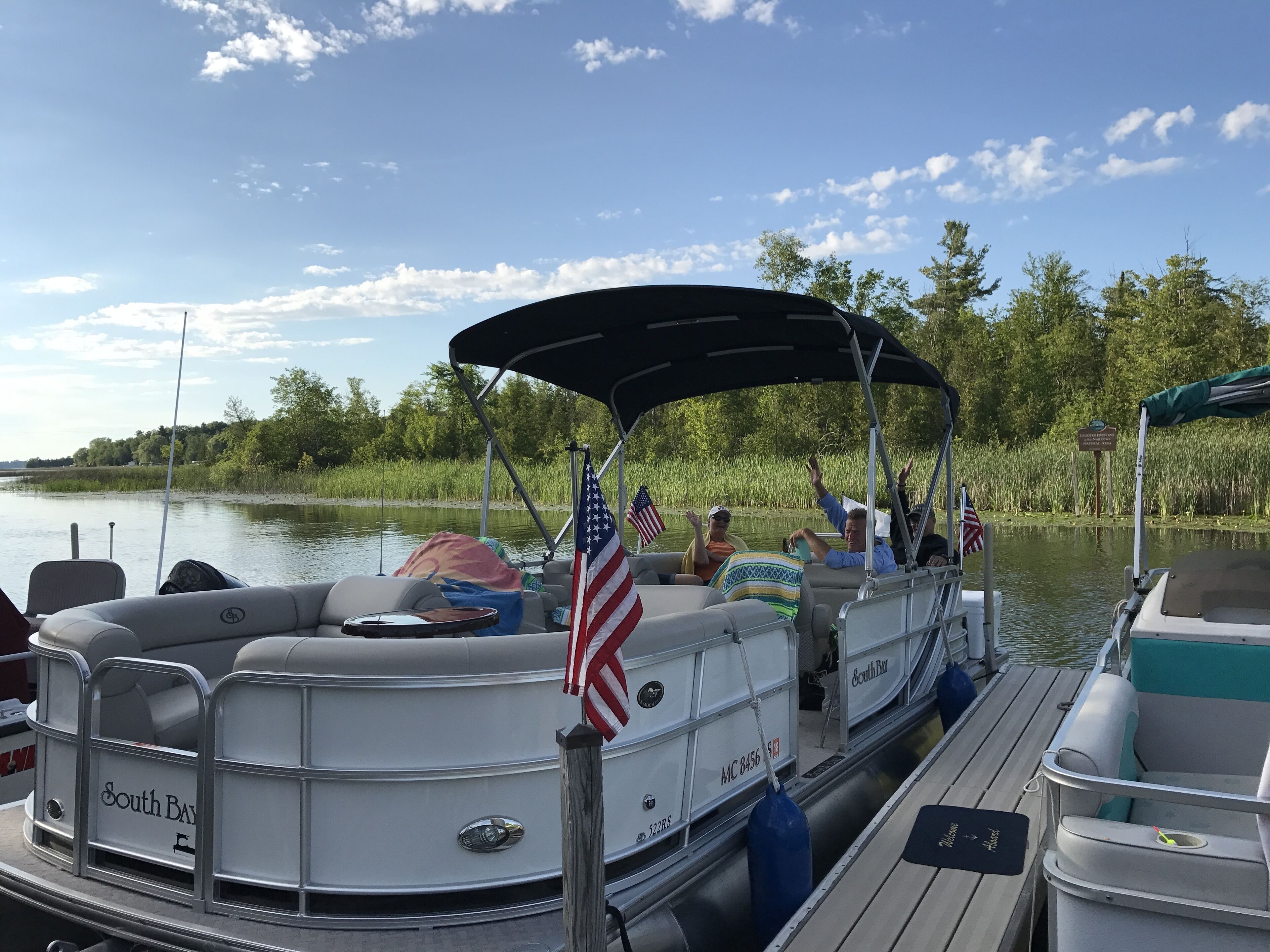 A boat docked at a pier with a covered seating area, American flags, and a sign indicating a fishing area.