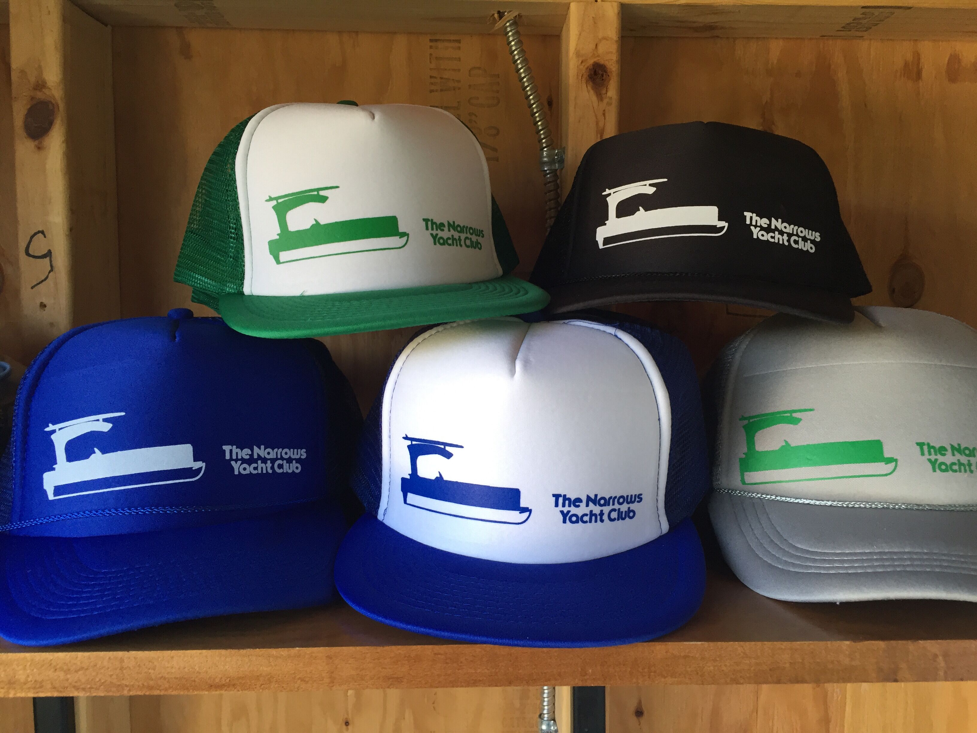 A wooden shelf with six caps from The Norries Yacht Club, each in different colors.