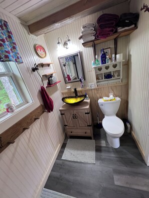 Une salle de bain avec un meuble-lavabo en bois, un lavabo avec un bac jaune, des toilettes blanches et un miroir au-dessus du lavabo.