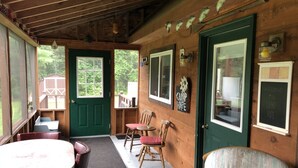 A rustic cabin interior with a wooden door, a small porch, and a table with chairs. - Secluded / Private Maine Lake Retreat,
WIR SPRECHEN DEUTSCH , (Burnham)