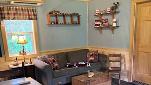 A cozy living room with a sofa, a wooden coffee table, a dining table with chairs, a lamp, and a window with plaid curtains. - Secluded / Private Maine Lake Retreat,
WIR SPRECHEN DEUTSCH , (Burnham)