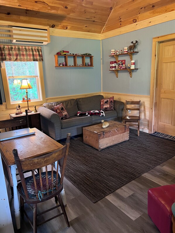 Una sala de estar acogedora con un sofá, una mesa de centro de madera, una mesa de comedor con sillas, una lámpara y una ventana con cortinas a cuadros.