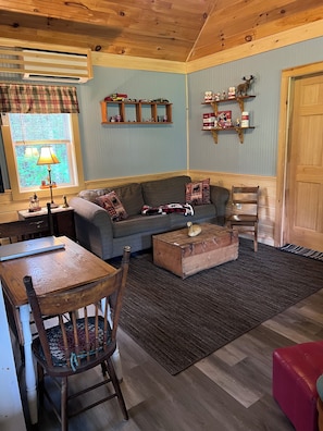 A cozy living room with a sofa, a wooden coffee table, a dining table with chairs, a lamp, and a window with plaid curtains. - Secluded / Private Maine Lake Retreat,
WIR SPRECHEN DEUTSCH , (Burnham)