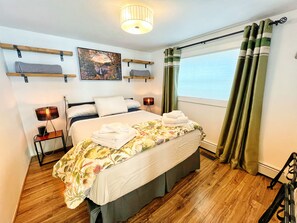 Una habitación de hotel ordenada con cama, lámparas de noche, un cuadro y una ventana con cortinas.