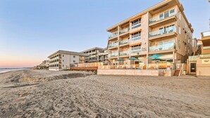 A beachfront hotel with multiple balconies, outdoor seating, and a sandy beach in the foreground. - OCEAN FRONT STUDIO ON THE SAND! (Carlsbad)