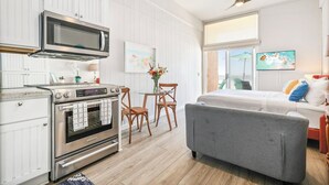 A compact kitchen with a microwave, oven, and dining area. There is a bed with a gray headboard and a window with a view. - OCEAN FRONT STUDIO ON THE SAND! (Carlsbad)