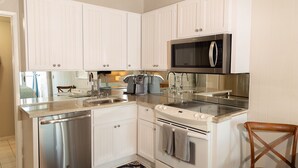 A compact kitchen with white cabinetry, stainless steel appliances, and a microwave. - OCEAN FRONT STUDIO ON THE SAND! (Carlsbad)