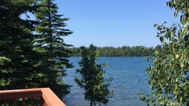 Eine Holzterrasse mit Blick auf einen ruhigen See, im Hintergrund dicht bewaldete Hügel.