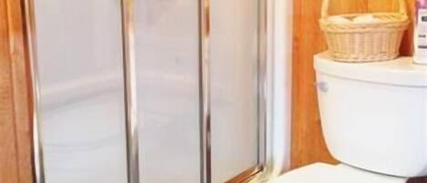 A bathroom with a glass-enclosed shower, a white toilet, and a wooden wall.