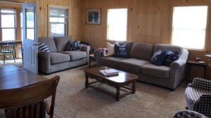 Ein gemütliches Wohnzimmer mit Holzwänden und -decke, einem grauen Sofa, einem Holztisch und einem karierten Sessel.
