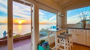 A kitchen with a view of the sea at sunset, a small bar area, and a window with a plant.