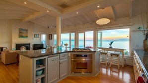 A spacious kitchen with a large island, a dining area with stools, and a view of the sea.