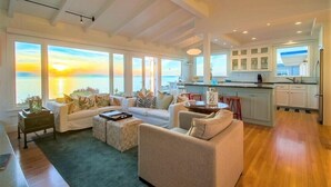 A spacious living room with a large window overlooking a scenic view, a cozy seating area, and a modern kitchen with white cabinets.