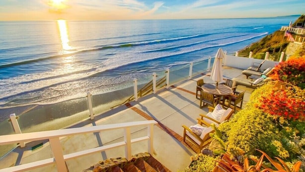 A coastal terrace with ocean views, outdoor seating, and a staircase leading down to the beach.