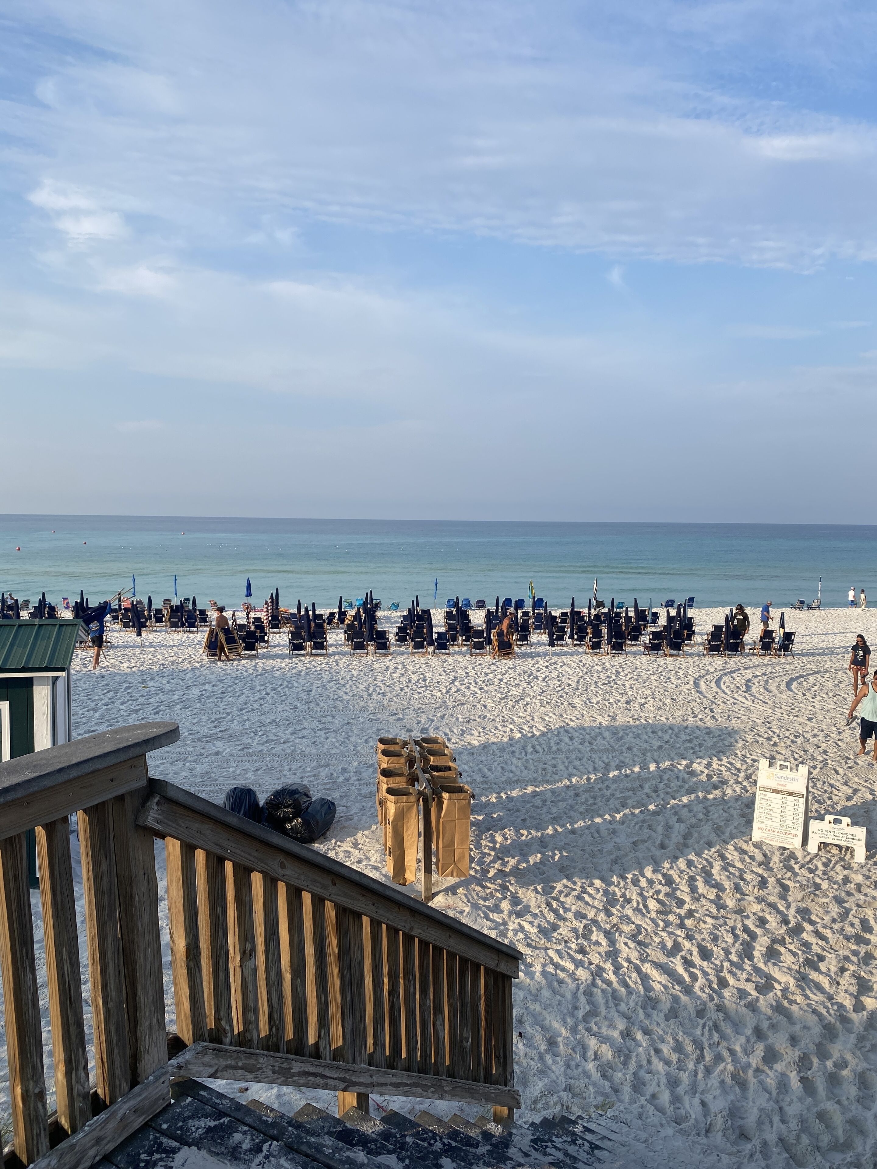 Une plage bordée de rangées de chaises de plage et de parasols, avec une terrasse en bois et une zone de plage sablonneuse.