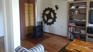 A living room with a sofa, a wooden coffee table, a bookshelf, a wall-mounted gear decoration, and a wood-burning stove. - Three Bedroom / Two Bath Beach House In The Heart Of Nye Beach (Newport)