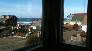 A view from a window overlooking a coastal street with houses and a beach. - Three Bedroom / Two Bath Beach House In The Heart Of Nye Beach (Newport)
