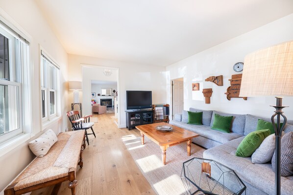 A living room with a sofa, a wooden coffee table, and a bench. There is a television and a lamp in the room. - Charming Farm House Downtown St. Helena! 3bedrooms/3baths
Permit # STR26-014 (St Helena)