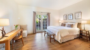 A bedroom with a bed, a desk, a chair, a bench, and a window with curtains. - Charming Farm House Downtown St. Helena!  3bedrooms/3baths
Permit # STR26-014 (St Helena)
