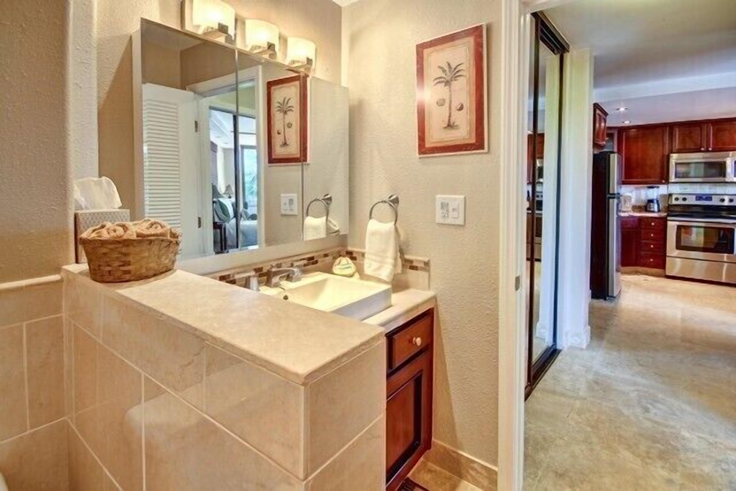 Une salle de bain avec un grand miroir, un lavabo et un meuble-lavabo. On y trouve un panier sur le comptoir et des serviettes accrochées au mur.