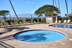 A pool area with two circular pools, lounge chairs, and a view of mountains. - Premier Ocean View! King Luxury Bed, A/C, Clean, Cozy, Updated, Wifi, Beach Gear (Kihei)