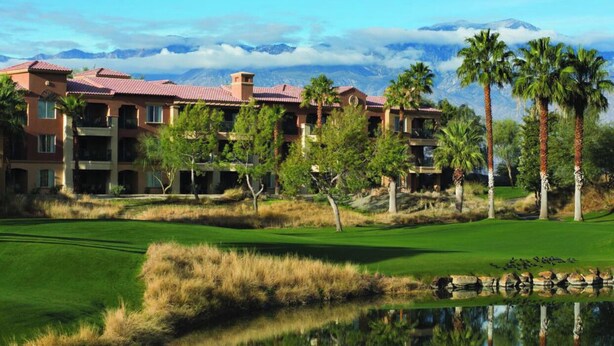 Un parcours de golf avec un étang, des palmiers et un bâtiment doté d’un toit rouge.