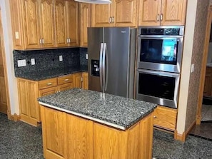 A kitchen with wooden cabinets, a granite countertop, a stainless steel refrigerator, and a double oven.