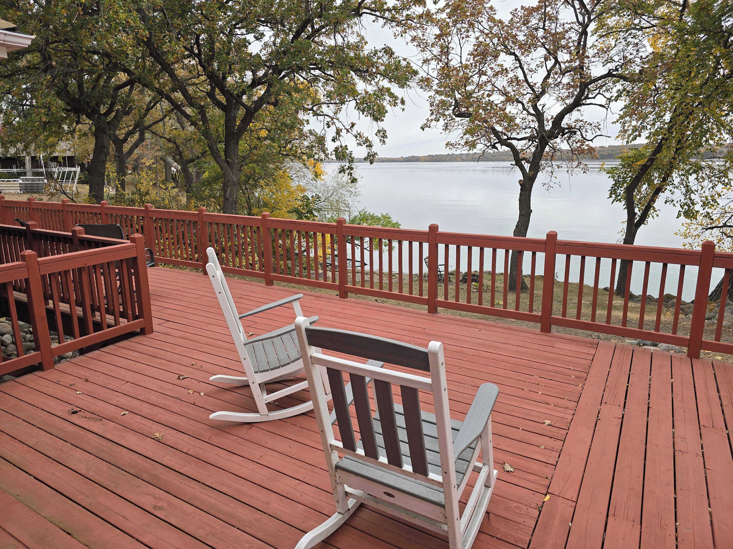 A wooden deck with rocking chairs overlooking a lake.