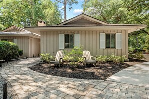 A two-story house with a covered porch, two Adirondack chairs, and a brick pathway leading to the entrance.