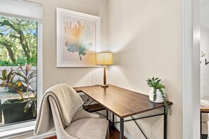 A room with a wooden desk, a chair, a lamp, a framed artwork, and a potted plant. - Serenity by the Sea – Pet-Friendly Sea Pines Home, Fenced Yard, Pool, Sleeps 8 (Hilton Head Island)
