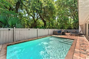 A rectangular pool with clear water, surrounded by a white fence, and a brick patio area with outdoor furniture.