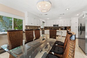 A modern kitchen with white cabinets, a glass dining table, wicker chairs, and a stainless steel refrigerator.