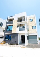 Un edificio residencial moderno de varios pisos con balcones, un garaje y fachada con tejas.
