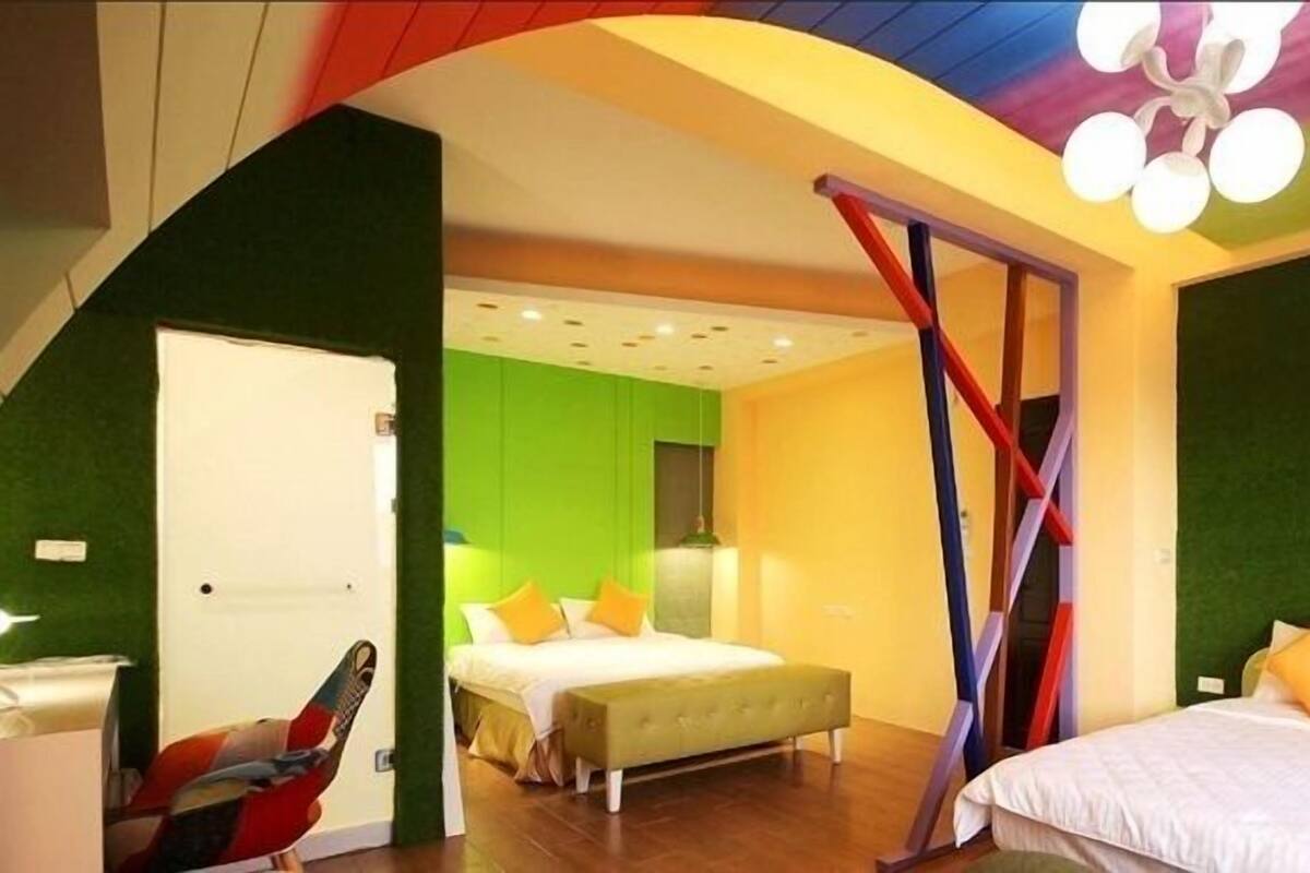 A modern hotel room with a green accent wall, a bed with white bedding and orange pillows, a bench, and a unique ceiling design.