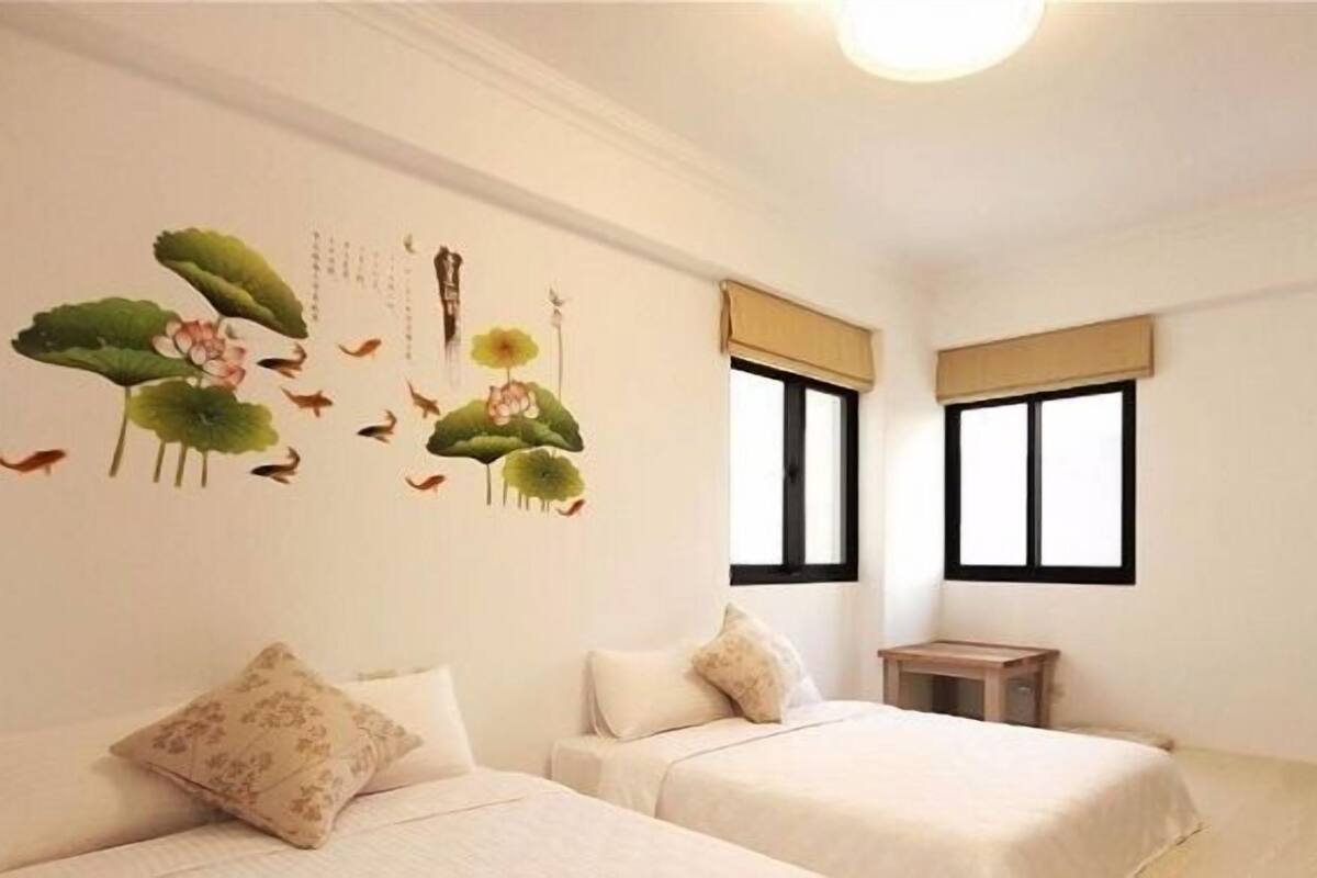 A hotel room with two beds, a small wooden side table, and a wall with a nature-themed mural.