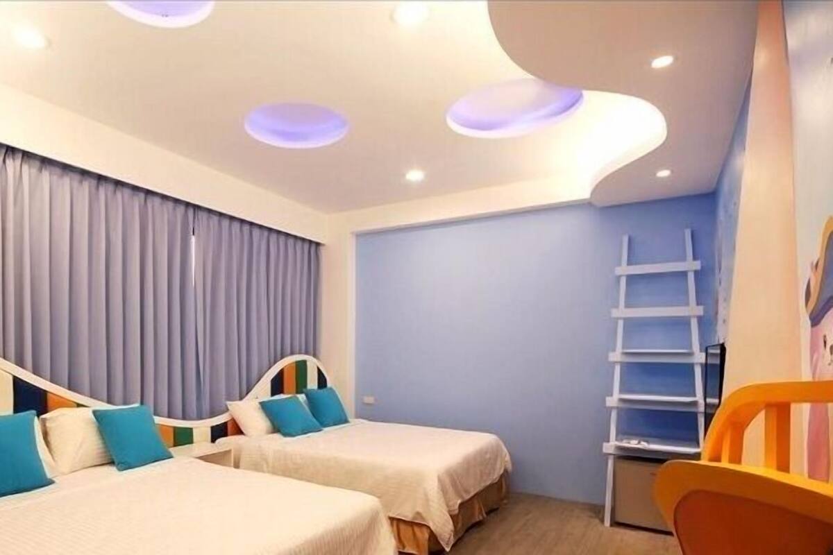 A hotel room with two beds, a window with curtains, a white headboard, a small ladder, and a colorful chair.