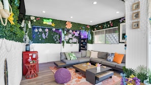Ein modernes Wohnzimmer mit grüner Wand, einem grauen Sofa, einem roten Kühlschrank und einem Holztisch.