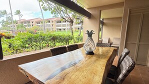 Une table à manger en bois avec des chaises, une lampe en forme d’ananas et une vue sur un bâtiment doté d’un toit rouge et de verdure.