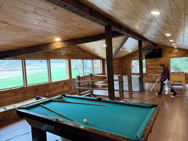 A pool table in a wooden room with large windows, a television, and a table tennis table.